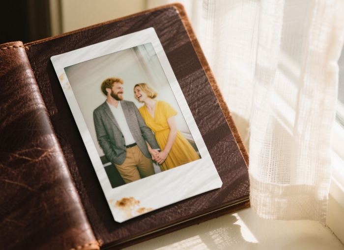 Leather-bound album open to a candid Polaroid of a couple laughing, coffee stains visible