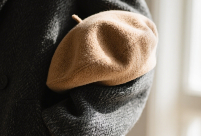 Luxuriously soft folded cashmere beanie in camel resting on grey wool coat sleeve
