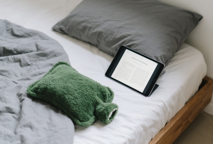 Plush-covered hot water bottle resting on fluffy bed