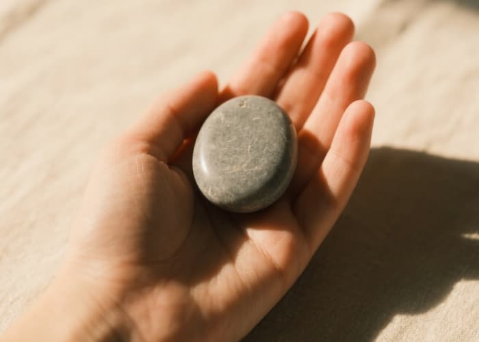 Close-up of a hand holding a smooth grey palm stone worry stone for anxiety grounding
